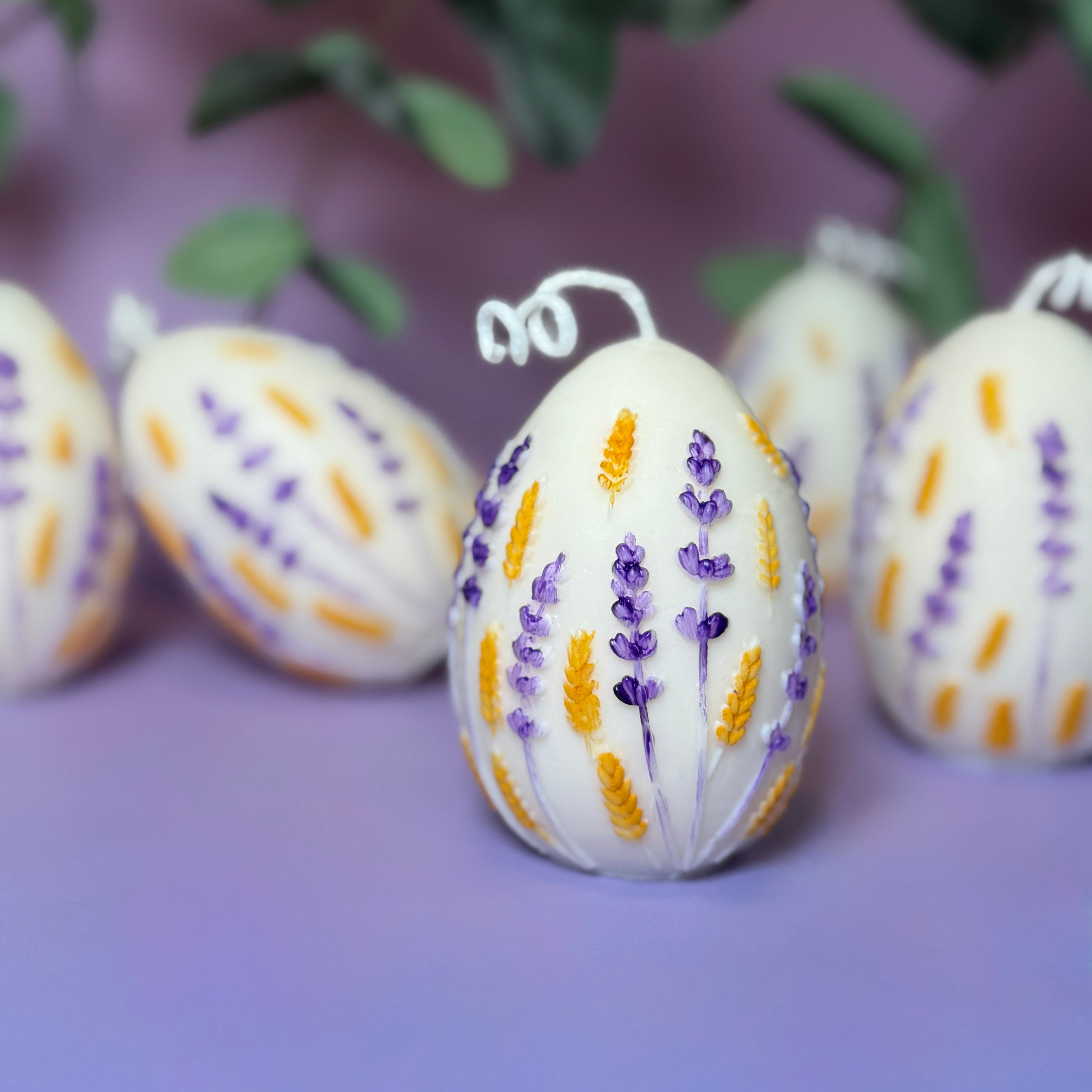 A collection of hand-painted harvest egg candles arranged against a soft background with green leaves, showcasing the consistency of the artisan hand-painted finish.
