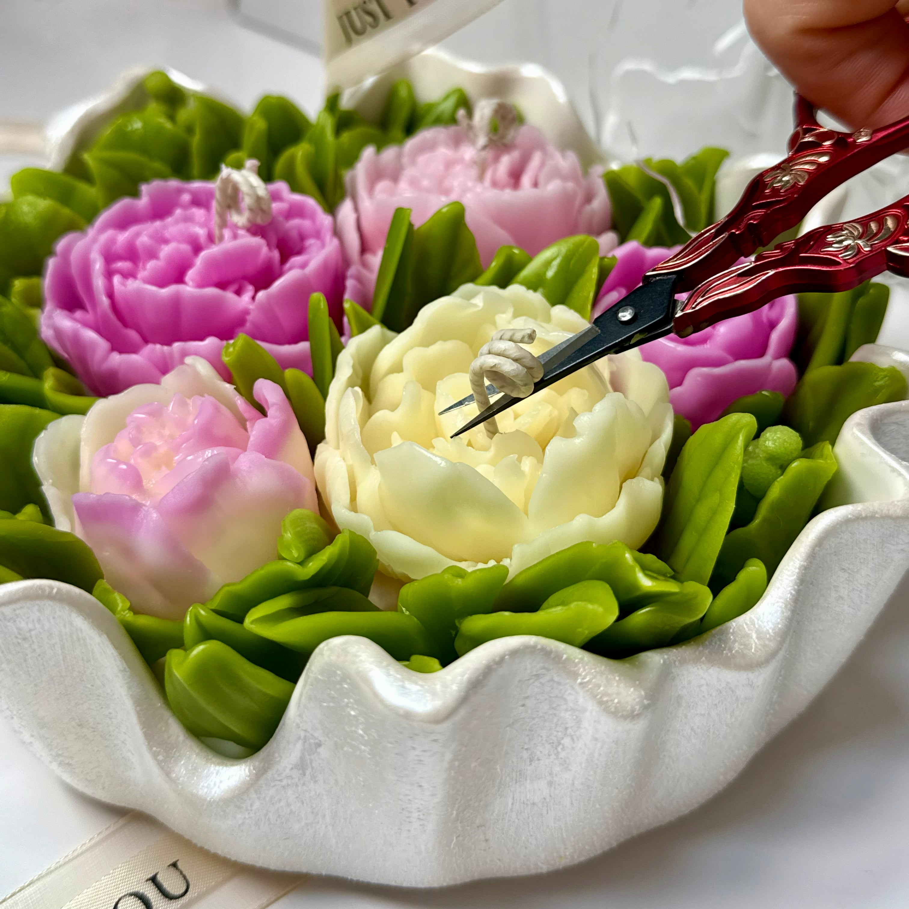 Decorative red vintage scissors trimming a cotton wick on a large 20cm hand-painted pearl white Jesmonite flower bouquet candle bowl.