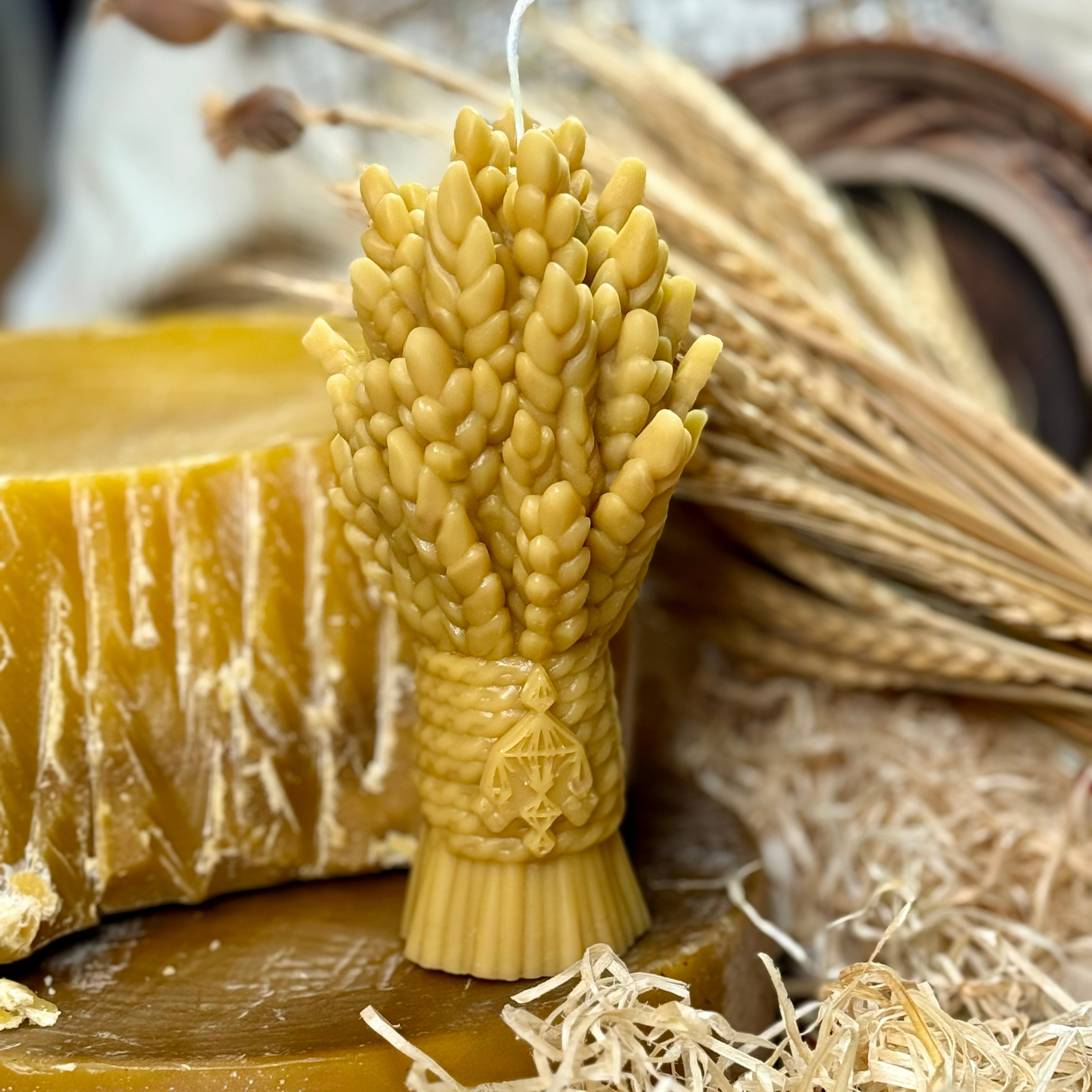 A front-facing view of the golden yellow pure beeswax Didukh candle moulded in the shape of a detailed wheat sheaf, showcasing the intricate ears of grain and a traditional heritage symbol on the bound base.