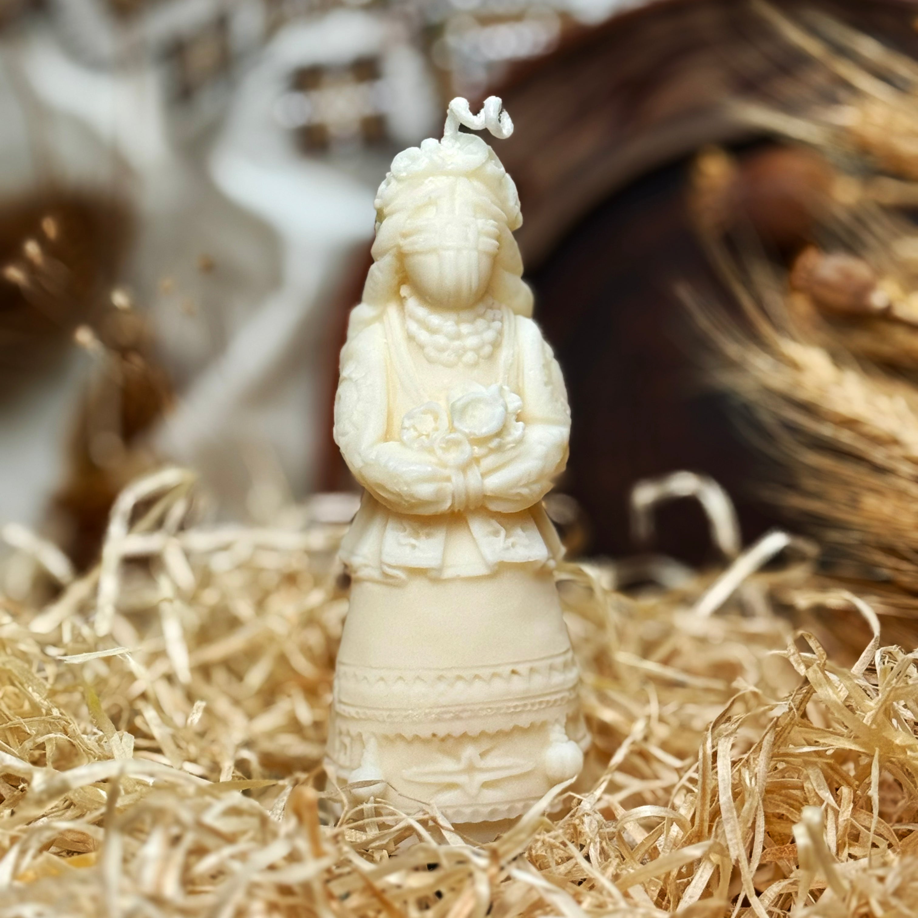 A close-up shot of the creamy ivory soy wax Motanka candle, beautifully capturing the intricate relief details of the faceless doll's traditional folk dress, beaded necklace, and floral crown.