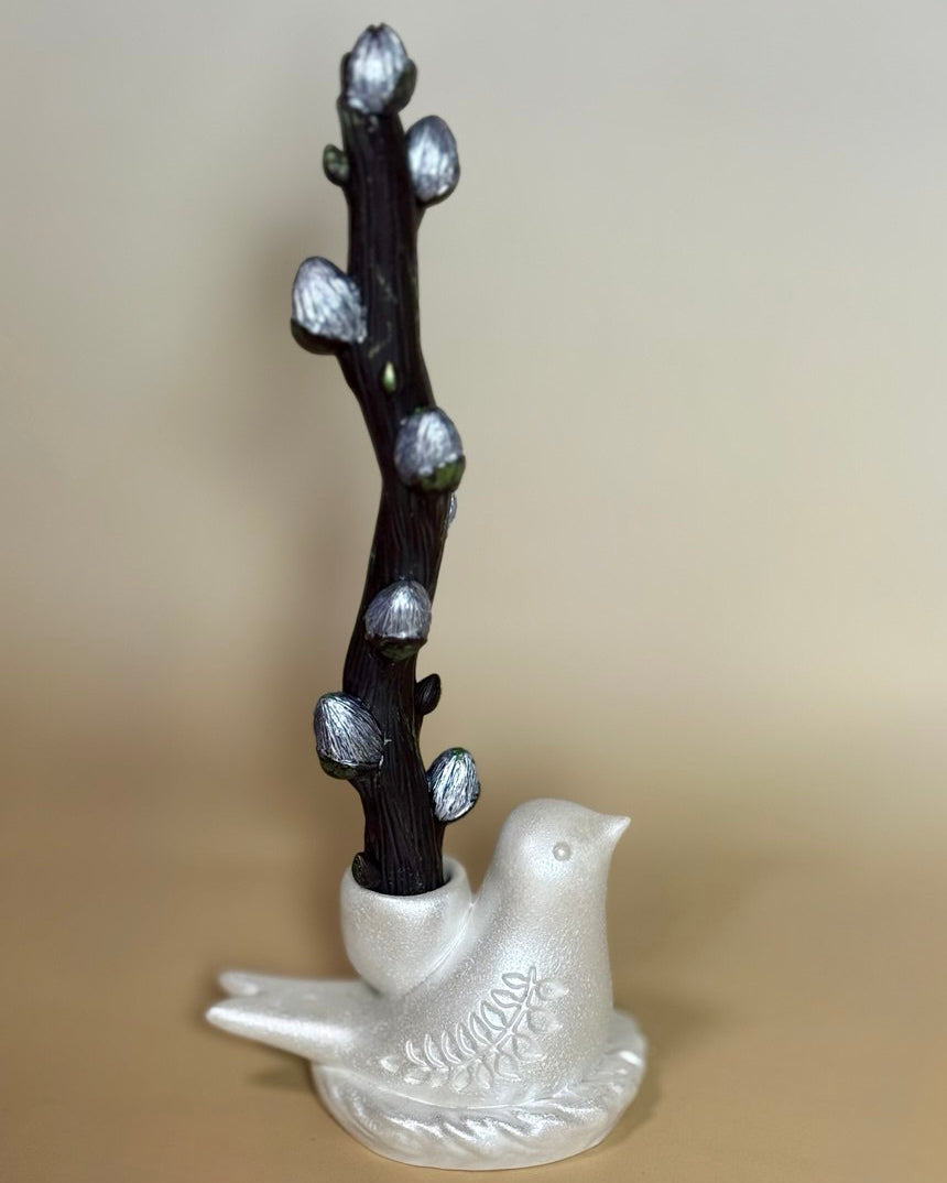 A dark sculptural beeswax willow branch candle displayed inside an unpainted pearl-white Jesmonite bird holder, showcasing the minimalist engraved leaf detailing on its side.