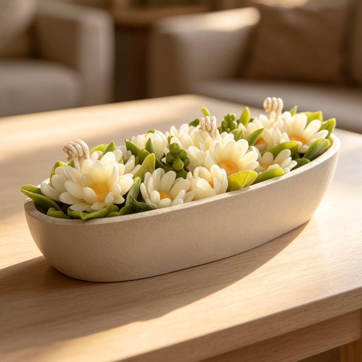An elegant oval daisy flower wax arrangement in a smooth white stone container, showcasing realistic yellow centres and green leaves under warm sunlight.
